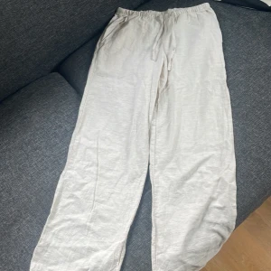 Beiga linnebyxor från Gina Tricot - Snygga och luftiga beiga linnebyxor från Gina Tricot med resår i midjan och dragsko. Byxorna har raka ben och sidfickor, perfekta för en chill och avslappnad stil. Materialet är 100% linne vilket gör dem superbekväma och svala.