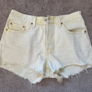 Levi's 501 gula jeansshorts med fransar - Snygga gula Levi's 501 jeansshorts med rå fransig kant och klassiska fem fickor. Shortsen har hög midja, bälteshällor och dragkedja med knapp. Perfekta för sommaren och ger en cool vintage vibe.