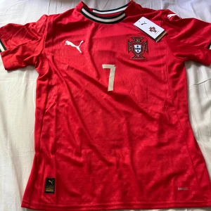Portugal Ronaldo 7 Puma fotbollströja S 2025 - Portugal landslagströja från Puma med Ronaldo och nummer 7 på ryggen. Röd med vita detaljer, broderat landslagsemblem och Puma-logga. Kortärmad modell i lätt och ventilerande material (Drycell). Ribbad krage med gröna och vita ränder. Jag säljer denna tröja då den var för liten för mig och går inte att lämna tillbaka eftersom den har brodering. Original pris 1450