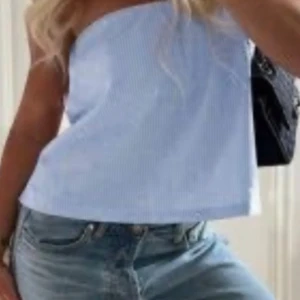 Ljusblå randig bandeau tubtopp - Säljer en ljusblå bandeau tubtopp med tunna vita ränder. Toppen är axelbandslös och har en avslappnad passform, perfekt till jeans eller kjol. Enkel och fräsch stil för varma dagar. Aldrig använt 