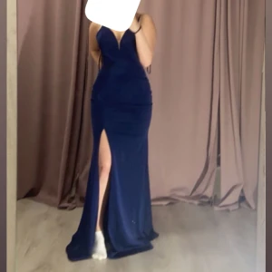 Marinblå långklänning med slits - Snygg marinblå långklänning med smala axelband och djup v-ringning. Klänningen har en hög slits framtill som ger en elegant och modern look. Figurnära passform som framhäver siluetten, perfekt för bal eller fest. Bilden var tagen innan klänningen var uppsydd så nu är den några cm kortare. Jag är 163 som referens och den är lagom lång i klackar🩵