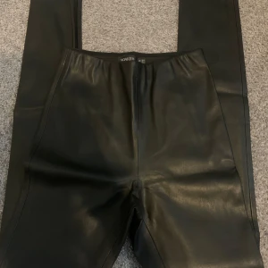 Svarta skinnleggings från Soaked in Luxury - Säljer ett par svarta leggings i skinnimitation från Soaked in Luxury. De har en tight passform och hög midja, vilket ger en snygg och stilren look. Perfekta att matcha med en oversized hoodie eller en cool t-shirt.