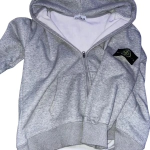Grå hoodie från Stone Island - Säljer en grå hoodie från Stone Island med dragkedja och klassisk logga på vänstra armen. Nästan oanvänd eftersom den var för liten har vanligtvis L.   Loggan är sne och det förväntas att köparen anser det och inte frågar om en retur när hen plockar upp den. 
