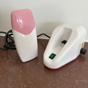 Elektrisk vaxvärmare rosa/vit - Elektrisk vaxvärmare i vit och rosa plast med laddningsstation och strömbrytare. Stationen kan i sin tur kopplas till en laddningstation. Perfekt för enkel och smidig applic  ering av vax med rullhuvud. Kommer med användarmanual på flera språk. Passar för hemmabruk. Vaxkassetten måste du skaffa själv.
