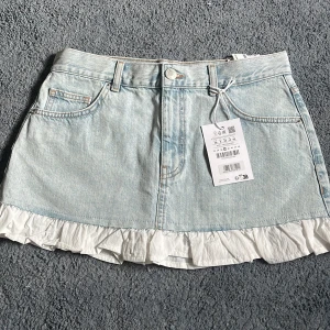 Ljus jeanskjol med volang - Jag säljer denna sjukt snygga jeanskjol med volang i vitt tyg. Älskar denna och den säljs då jag beställde den i flera olika storlekar, varav denna var en av dem som var för stora (och jag tappade bort returneringsetiketten så kunde ej returnera till butiken). Därför säljer jag den på Plick. Men den är ALDRIG ANVÄND och därför i ny skick. Kjolen har dragkedja och knapp framtill.