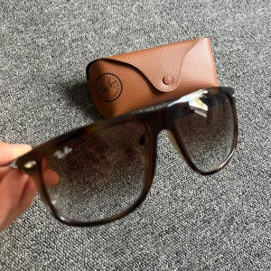 Bruna Ray-Ban RB4147 solglasögon - Snygga Ray-Ban RB4147 solglasögon med brunmelerad plastbåge och stora, fyrkantiga glas. Ljusbruna tonade linser och klassisk logga på linsen. Kommer med original Ray-Ban-fodral i brunt. Perfekta för att lyfta din stil i solen.