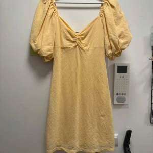 Gul kort klänning med puffärm BikBok - Supersöt ljusgul kort klänning från BikBok med puffiga korta ärmar, v-ringning och snörning i ryggen. Klänningen har en lätt struktur i tyget och är perfekt för varma dagar eller nu på midsommar. Säljer då den inte kommer till användning längre, använd endast en gång😋