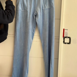 Ljusblå mjukisbyxor Juicy Couture - Supermysiga ljusblå mjukisbyxor från Juicy Couture med broderad JC-logga framtill. Byxorna har raka ben, bred resår i midjan. 