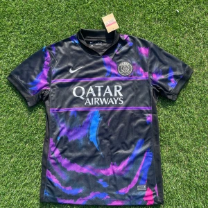 PSG x Nike svart fotbollströja L - Paris Saint-Germain fotbollströja från Nike i svart med lila och blå detaljer. Tröjan har korta ärmar, rund hals och är tillverkad i Dri-FIT-material som andas. PSG-logga och Nike Swoosh broderade på bröstet, samt Qatar Airways-tryck på magen.