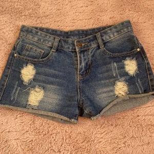 Blå slitna jeansshorts med uppriven look - Snygga blåa jeansshorts med slitna detaljer och uppriven look framtill och baktill. Klassisk femficksmodell med uppvikta benslut och bälteshällor. Perfekta för sommaren när det är riktigt varmt! W26