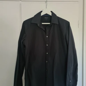 Svart skjorta från Tiger of Sweden - Snygg svart skjorta från Tiger of Sweden i slim fit. Tillverkad i 100% bomull med klassisk krage och knappar framtill. Perfekt för en stilren look.