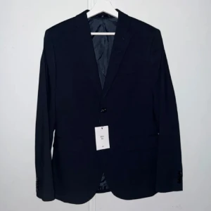 Mörkblå kavaj - Elegant mörkblå kavaj med klassisk design från hm. Perfekt för formella tillfällen. Kavajen har en enkelknäppt stil med två knappar framtill och fickor på sidorna. Passar utmärkt för en stilren look. Storlek 46. Den är helt ny och aldrig använd. Nypris 499kr. 
