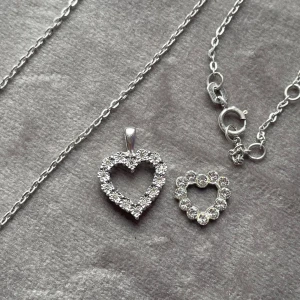 Halsband med hjärtformade hängen i äkta silver - Säljer ett fint halsband med två hjärtformade hängen i äkta silver, dekorerade med glittrande stenar. Perfekt accessoar för att ge en extra touch till din outfit. Kedjan är tunn och elegant.