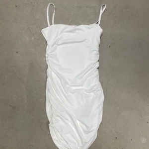 Vit satin klänning med smala axelband från SHEIN - Säljer en vit, figurnära klänning från SHEIN i satinliknande material. Klänningen har smala axelband och en enkel, elegant design med lätt rynkade detaljer längs sidorna. Perfekt för dig som gillar minimalistisk stil.