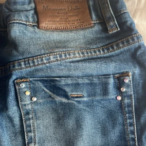 Jeanskjol från Massimo Dutti - Säljer en klassisk blå jeanskjol från Massimo Dutti med fickor fram och bak samt bälteshällor. Kjolen har en knapp i midjan och dekorativa nitar på bakfickorna.