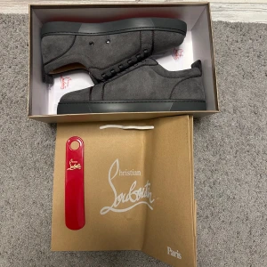 Grå sneakers från Christian Louboutin - Säljer ett par stilrena grå sneakers från Christian Louboutin. Skorna har en rund tå och är tillverkade i mocka med klassisk röd sula. De har snörning och kommer med en röd skohorn. Perfekta för den som vill ha en touch av lyx i vardagen. Priset är inte hugget i sten! Kom privat för fler frågor :)