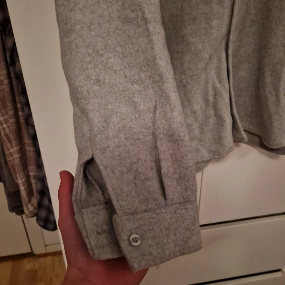 Säljer en stilren grå overshirt med knappar framtill. Den har en klassisk krage och är tillverkad i ett mjukt material som ger en bekväm känsla. Perfekt för en fet grisch stil💯. Neuletakit & Villapaidat.