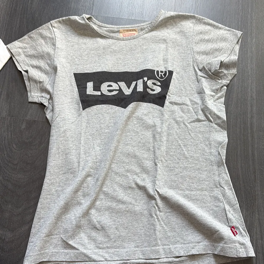 Säljer en grå t-shirt från Levi's med deras logga tryckt i svart på framsidan. T-shirten är kortärmad och tillverkad i bomull. Tröjan är väl använd men ingenting som syns, är väldigt oklar på storlek då det inte står, men skulle säga att de är runt stl 164. T-paidat.