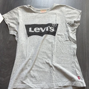 Grå t-shirt från Levi's - Säljer en grå t-shirt från Levi's med deras logga tryckt i svart på framsidan. T-shirten är kortärmad och tillverkad i bomull. Tröjan är väl använd men ingenting som syns, är väldigt oklar på storlek då det inte står, men skulle säga att de är runt stl 164