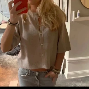 Beige kofta med kort ärm och knappar - Säljer en beige kofta med korta ärmar och ribbade kanter.Super fint sick och knappast använd. Perfekt att slänga över sig nu till sommaren🌸