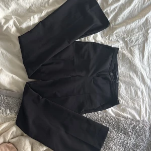 Svarta kostymbyxor från Gina Tricot - Säljer ett par svarta kostymbyxor från Gina Tricot i storlek XS. Byxorna har utsvängda ben, pressveck och stängs med dragkedja och knapp. Klassisk design med fickor bak och normal passform.
