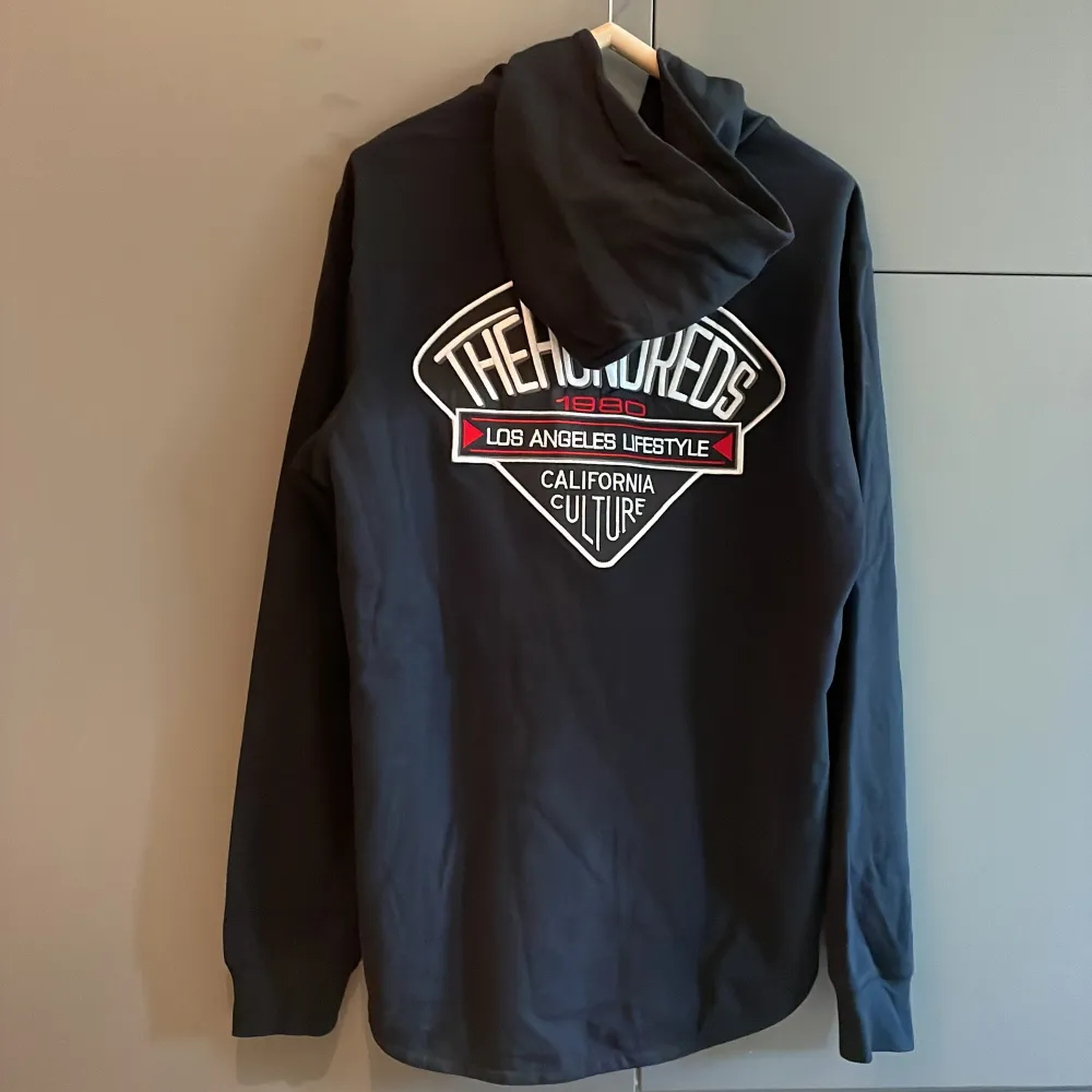 Säljer en svart hoodie från The Hundreds med tryck både fram och bak. Hoodien har en stor ficka framtill och en huva. Perfekt för en avslappnad stil. 🖤. Hupparit & Collegepaidat.