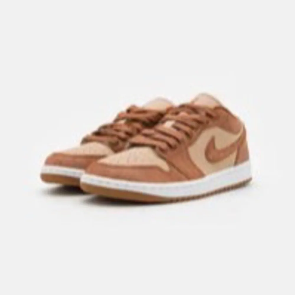 Snygga Nike Air Jordan 1 low i en stilren kombination av brunt och beige. Skorna har en klassisk design med snörning och rund tå. Perfekta för dig som vill ha en sportig och trendig look. Storlek 39. Kengät.