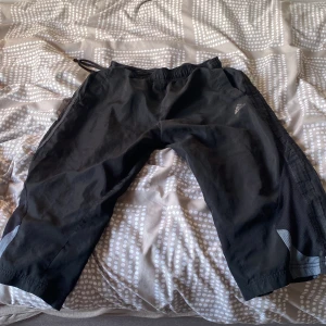 Svarta träningsbyxor från Adidas - Svarta träningsbyxor från Adidas med ClimaCool-teknologi. Byxorna har resår i midjan, reflexdetaljer vid benen och är trekvartslånga. Perfekta för träning eller sportaktiviteter. Adidas-logga på vänster lår.