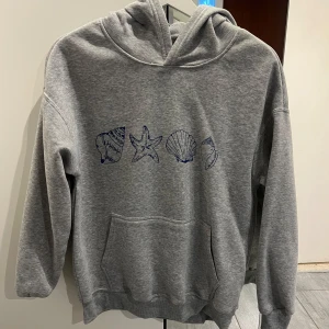 Grå hoodie med snäckmotiv - Grå hoodie med blåa snäckmotiv framtill. Aldrig använd