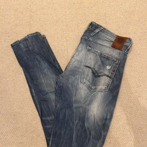 Replay anbass  - Säljer ett par blå jeans från Replay med slitningar och ljusa tvättade partier. Perfekta för en avslappnad och trendig look.