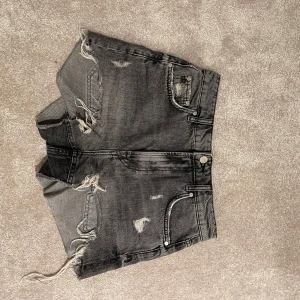 Svarta jeansshorts från Zara - Säljer ett par coola svarta jeansshorts från Zara med slitna detaljer och fransar. De har en klassisk femficksdesign och är perfekta för en avslappnad stil. Passar utmärkt till sommarens alla äventyr!