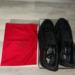 Svarta sneakers från Valentino Garavani - Snygga svarta sneakers från Valentino Garavani med klassisk snörning och diskret logga på plösen. Skorna har en robust sula med bra grepp och kommer med en röd förvaringspåse. Perfekta för en stilren look.