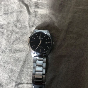 Silverfärgad klocka från Festina - Snygg och stilren klocka från Festina med en silverfärgad länkarmband och svart urtavla. Klockan har datumvisning och en klassisk design som passar perfekt för alla tillfällen. Den är tillverkad i rostfritt stål och har en elegant finish.