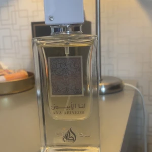 Ana Abiyedh (Erba Pura) - Ana Abiyedh Eau de Parfum från Lattafa i en elegant rektangulär flaska med vit kork. Parfymen är tillverkad i U.A.E. och har en volym på 80%. Flaskan har en dekorativ etikett med ett intrikat mönster.