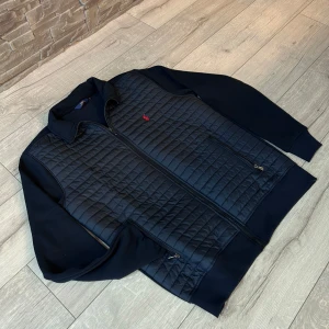 Mörk blå Ralph lauren cardigan  - Säljer en svart quiltad jacka från Polo Ralph Lauren med dragkedja och två fickor framtill. Jackan har långärmade partier i mjukare material och klassisk krage. Liten röd logga broderad på bröstet. Perfekt för kyliga dagar. Passar L också 😁