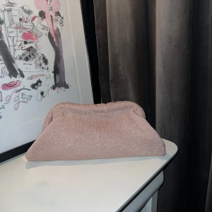 Glittrig rosa kuvertväska - Säljer en superfin clutch väska i glittrigt rosa material. Väskan är från mitt uf företag Válorie och är handsydd av oss i företaget av återanvända tyger. 