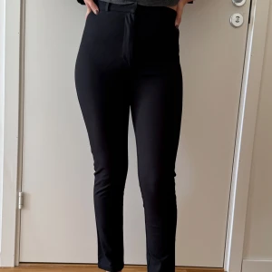 Avora Byxor storlek 36 - Snygga svarta byxor med tight passform och hög midja. Perfekta för en stilren look. Byxorna har en enkel design utan mönster eller extra detaljer.