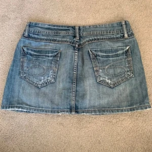 Jeanskjol från Miss Sixty - Snygg jeanskjol från Miss Sixty i en klassisk blå tvätt. Kjolen har femficksdesign med två bakfickor och en knapp- och dragkedjestängning fram. Perfekt för en avslappnad stil!