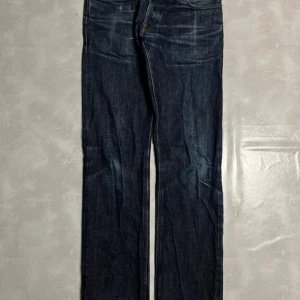 Japanese selvegde raw denim - Snygga blå råa jeansbyxor med en klassisk femficksdesign i storlek Waist: 32 Length: 34 Med tanke på att de är råa så ändras faden och färgen över tid med användning. De har en normal passform och är perfekta för en avslappnad stil. Byxorna har en blixtlåsgylf och är tillverkade i slitstarkt denim.