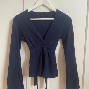 Mörkblå topp från Gina Tricot - Säljer en mörkblå topp från Gina Tricot i storlek XS. Toppen har långa ärmar, v-ringning och knytband i midjan. Perfekt för dig som gillar en stilren och enkel look. Använd en gång så är precis som ny💗