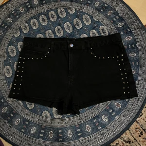 Svarta shorts med nitar från Forever 21 - Snygga svarta shorts från Forever 21 med coola nitar längs sidorna. Perfekta för en edgy look. står storlek 44 och jag rekommenderar på strl M/L