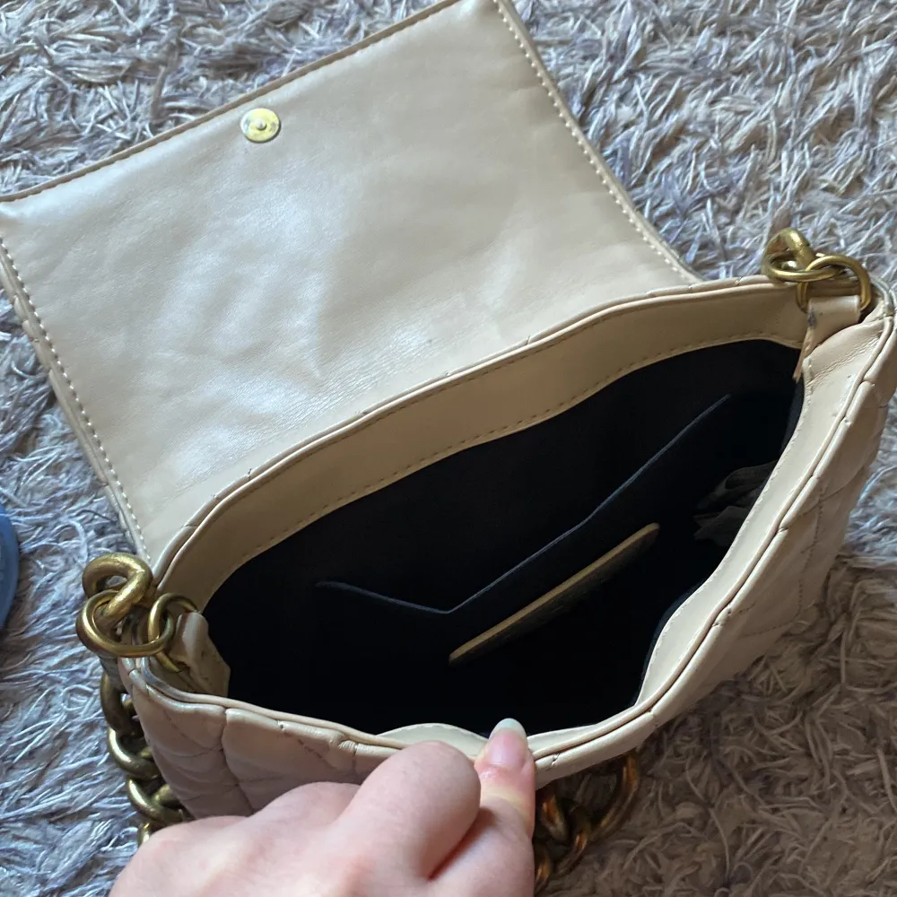 Snygg beige axelväska med quiltat mönster och en rejäl guldfärgad kedja som axelrem. Väskan har ett praktiskt magnetlås och ett rymligt inre fack. Perfekt för att ge din outfit en stilfull touch. Kan gå ner i pris vid snabb affär💖. Laukut & Käsilaukut.