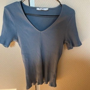 Blå ribbad topp från NA-KD - Säljer en snygg blå ribbad topp från NA-KD med v-ringning. Toppen har korta ärmar och en skön passform. Perfekt för en stilren look!