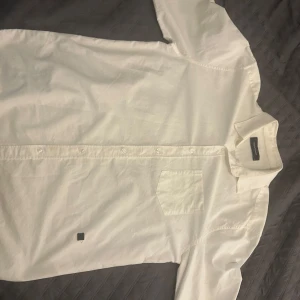 Vit skjorta från Peak Performance - Säljer en stilren vit skjorta från Peak Performance i storlek XL. Skjortan har långs ärmar och en klassisk krage med knappar framtill. Perfekt för en avslappnad men ändå uppklädd look.