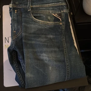 Blå Replay Anbass jeans slim fit - Säljer ett par blå Replay Anbass jeans i slim fit-modell. Klassisk femficksdesign med snygga slitningar och Replay-logga på fickan. Jeansen har normal passform och är tillverkade i denim med lätt stretch för extra komfort.