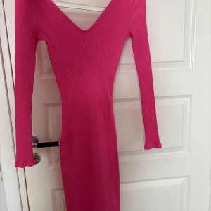 Rosa ribbad klänning från NA-KD - Snygg rosa ribbad klänning från NA-KD med en v-ringad design. Klänningen har långa ärmar och en figurnära passform som framhäver silhuetten. Perfekt för en stilren look.