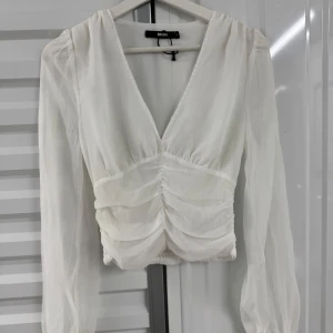 Vit blus med v-ringning från Bik Bok - Säljer en helt ny vit blus från Bik Bok med v-ringning och långa ärmar. Blusen har rynkade detaljer framtill och är tillverkad i ett lätt, tunt material. Perfekt för en stilren och trendig look.
