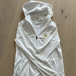 Vit hoodiejacka från Nike med franska landslagets emblem - Säljer en vit hoodiejacka från Nike med dragkedja och huva. Använd två gånger. Tröjan är köpt ifrån Nike. Självklart äkta. Pris kan diskuteras. Köpt för ca 1000kr