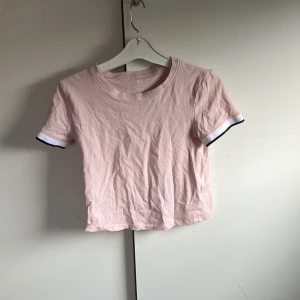 Ljusrosa croppad t-shirt från H&M - Säljer en ljusrosa croppad t-shirt från H&M Basic i ekologisk bomull. T-shirten har korta ärmar med vita och svarta detaljer vid ärmsluten. Enkel och stilren modell som passar perfekt till jeans eller kjol. Storlek 158/164. 