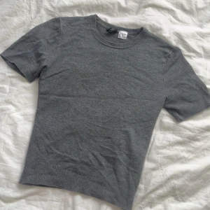 Grå kortärmad tröja från H&M - Säljer en stilren grå kortärmad tröja från H&M. Perfekt för en avslappnad look. Tröjan har ribbade kanter vid ärmslut och nederkant.